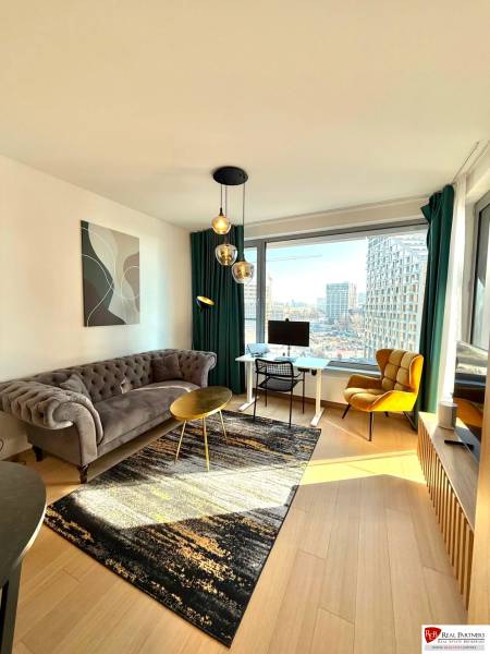 A bright living room with a sofa and wood-patterned flooring in a two-room apartment.