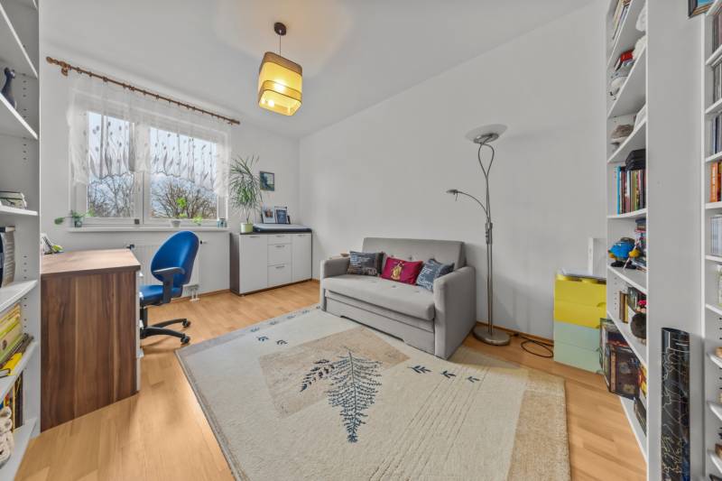 A study in a 4-room apartment with a sofa, carpet, blue chair, and a wooden-patterned floor.