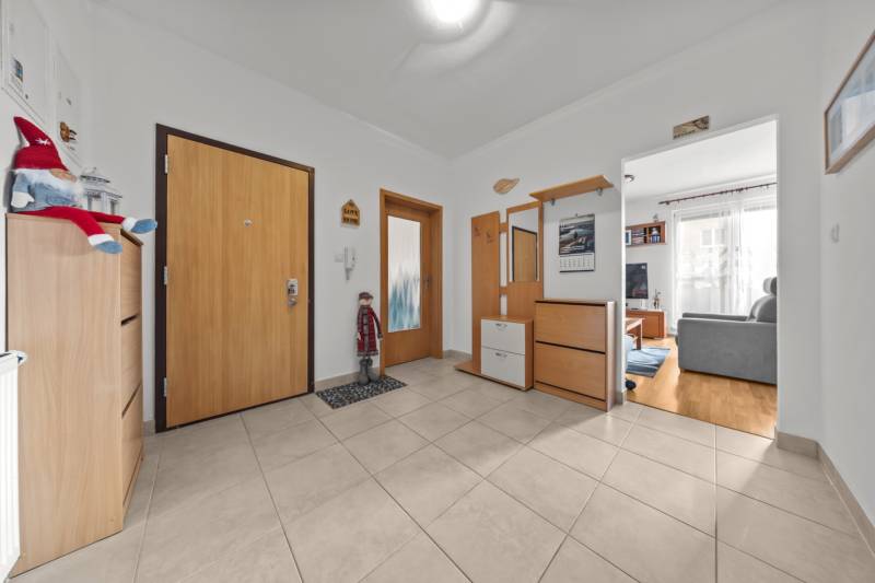A hallway in a 4-room apartment with a living room, light-colored walls and decorations, and a floor with a wooden decor.