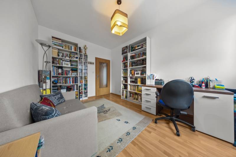 A room in a 4-room apartment with a library, a desk, a sofa, and a floor with a wooden decor.