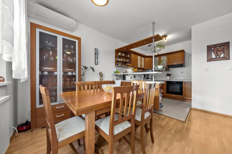 Dining area with wooden furniture and a kitchen in a 4-room apartment with a wood-patterned floor.