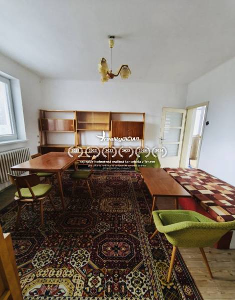 A family house with antique furniture, a carpet with colorful patterns, and green chairs.