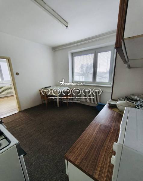 A kitchen with a gas stove and carpet in a family house, white interior, table, window with blinds.