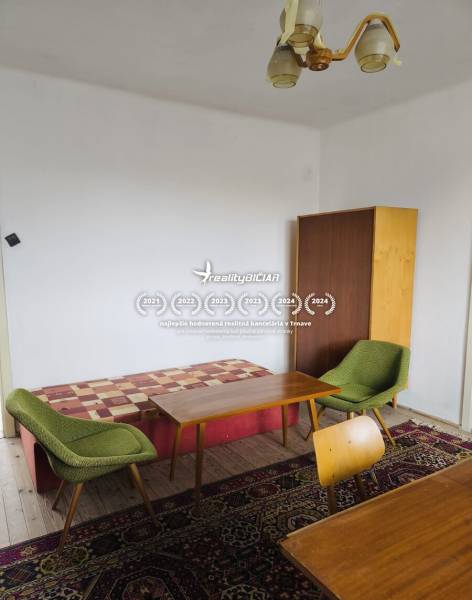 A room of a family house with armchairs, tables, a cabinet, and a wooden-patterned floor.