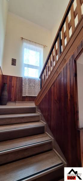 Stairs in a family house with wooden paneling, a railing, and a window with a lace curtain.