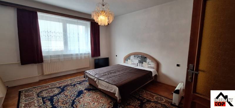 A bedroom in a family house with a bed, a chandelier, and a carpet on a floor with a wooden decor.