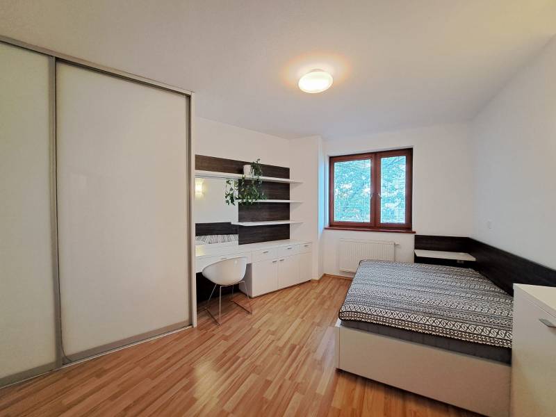 Bedroom in a two-room apartment with a wood-patterned floor and a desk.