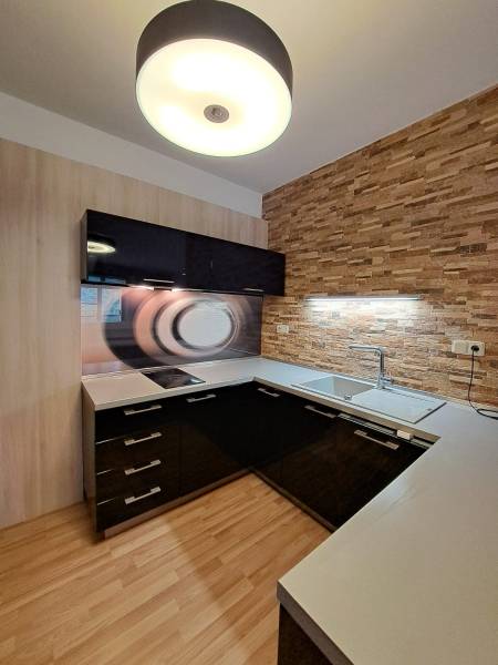 A kitchen in a 2-room apartment with a wooden decor floor and brick cladding on the wall.