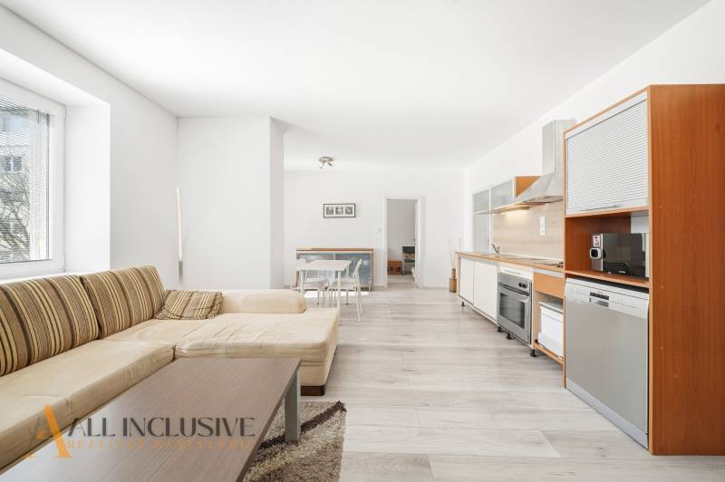 Spacious living room with kitchen, wooden decor flooring, large sofa.