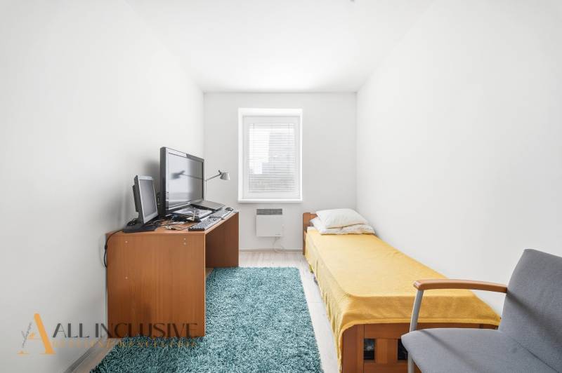 A room with a single bed, carpet, and a desk with a computer in a 3-room apartment.