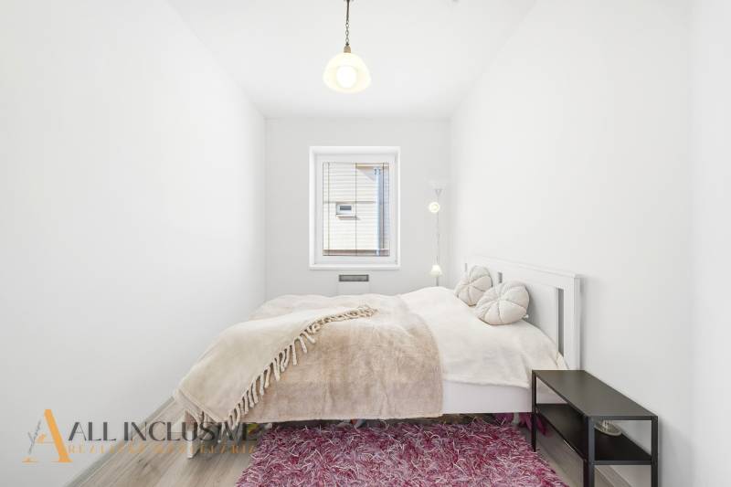 A bright bedroom with a light bed, a pink carpet, and a wood-patterned floor.