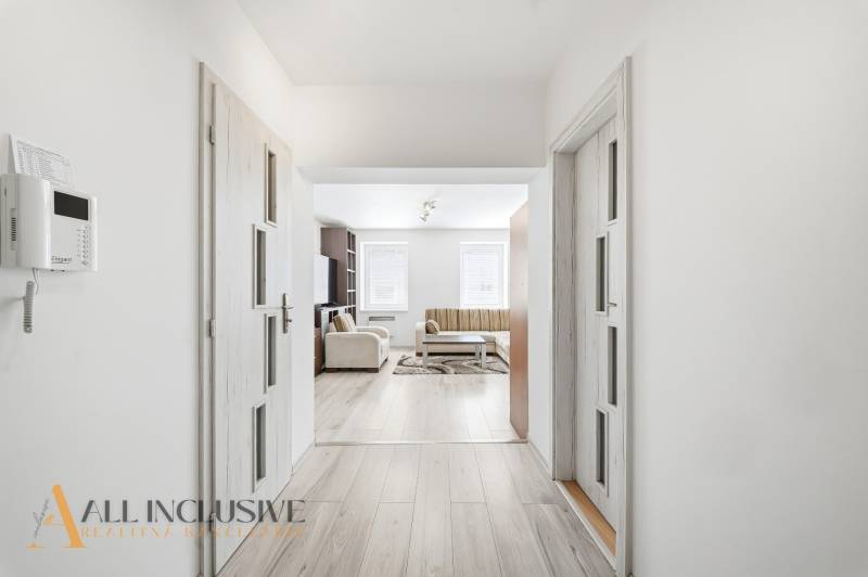 Bright hallway in a 3-room apartment with wood-patterned flooring and a sofa in the living room.