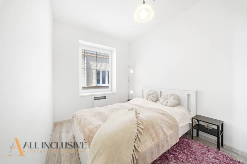 Bright bedroom with a bed, lamp, and window, 3-room apartment with wood-patterned flooring.