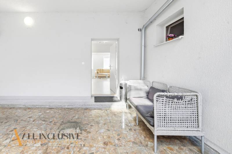 A white room with wicker seating next to a gray door leading to a 3-room apartment.