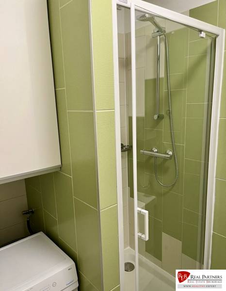A shower corner in a bathroom with green tiles and a washing machine in a 2-room apartment.