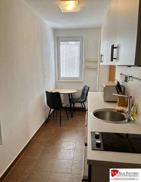 A kitchen in a 2-room apartment with a sink, stove, and a table with chairs.