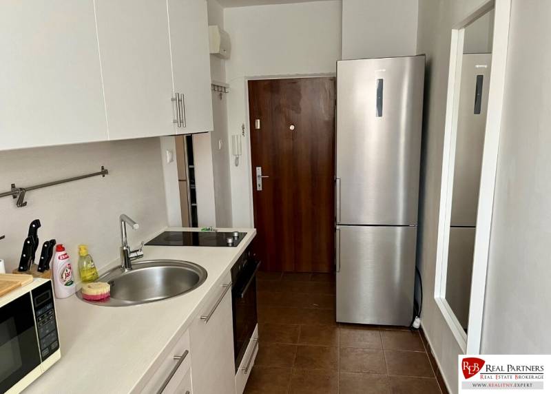 A kitchen with white cabinets, a sink basin, and a stainless steel refrigerator in a two-room apartment.