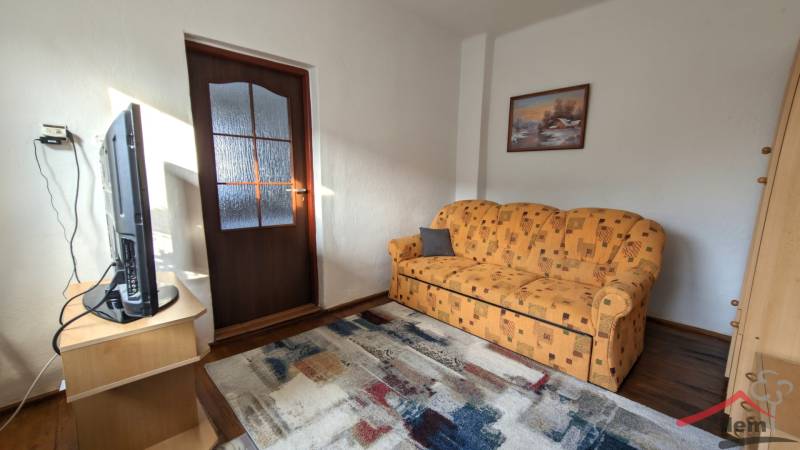 Living room with an orange sofa and a television, wooden decor flooring, family house.