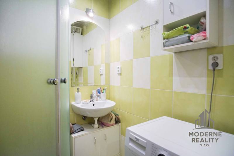 Bathroom in a 2-room apartment with a sink, washing machine, and green tiles.