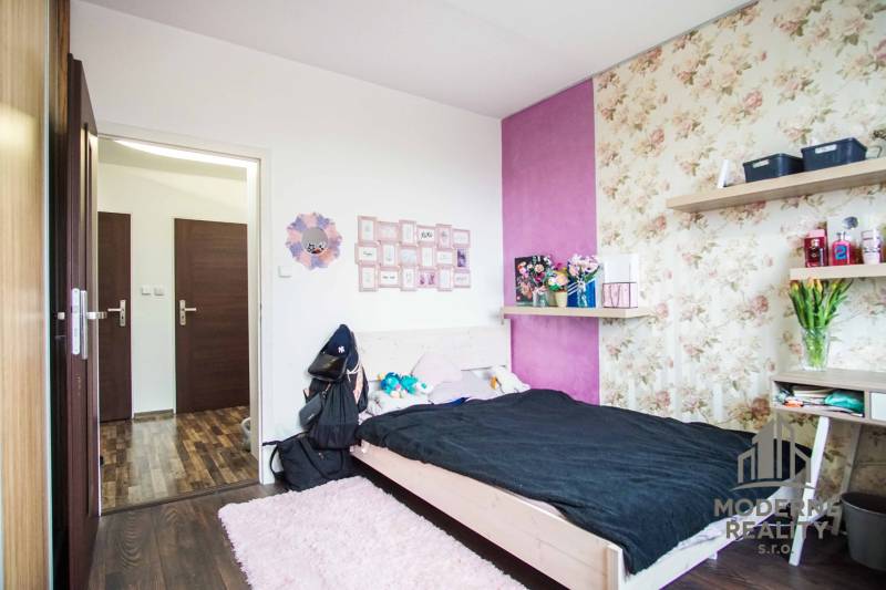 A bedroom in a two-room apartment with floral wallpaper and a wooden decor floor.