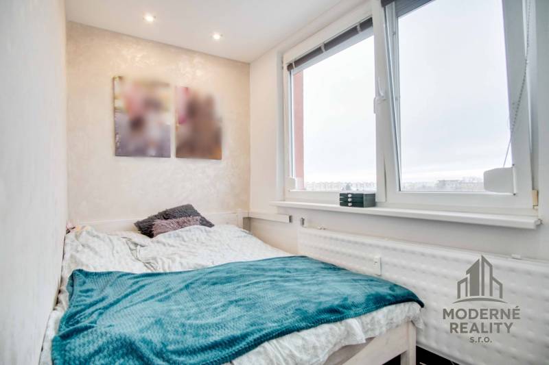 Bedroom in a two-room apartment with a bed, blanket, and large window.