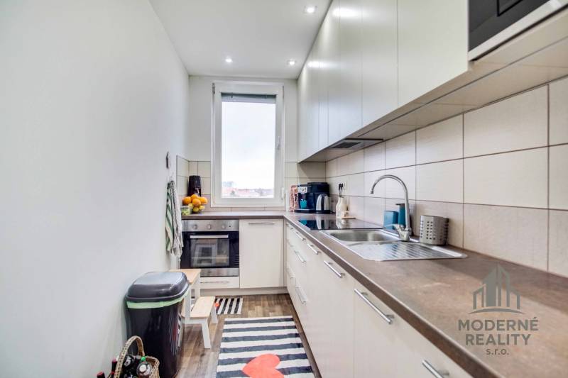 A kitchen in a 2-room apartment with a wooden decor floor and stylish cabinets.