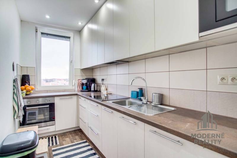 A kitchen in a 2-room apartment with a window, built-in oven, and floor with wood decor.