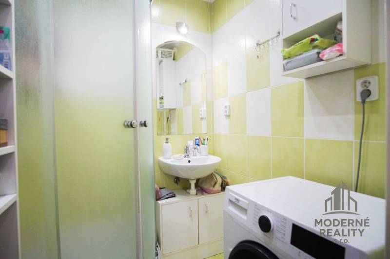 A bathroom in a 2-room apartment with a shower, sink, and washing machine.
