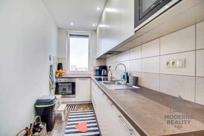 A kitchen in a 2-room apartment with a wooden floor decor and white cabinets.