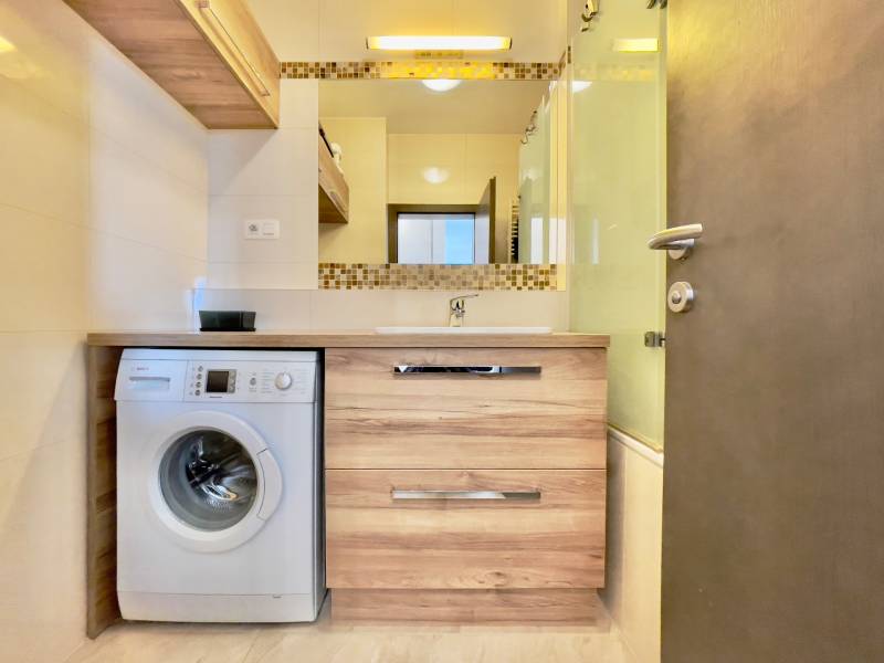 Bathroom with a washing machine and a sink in a 3-room apartment, floor with wood decor.