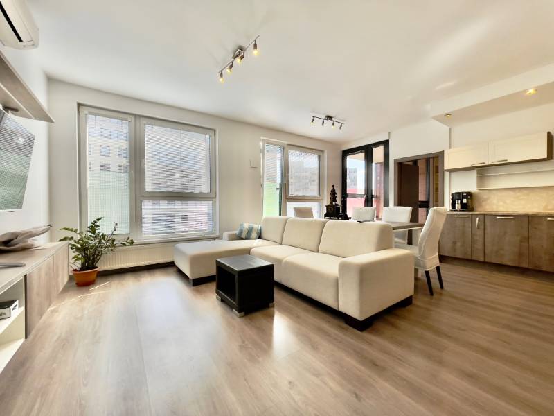 A bright living room with wood-patterned flooring and comfortable seating in a three-room apartment.