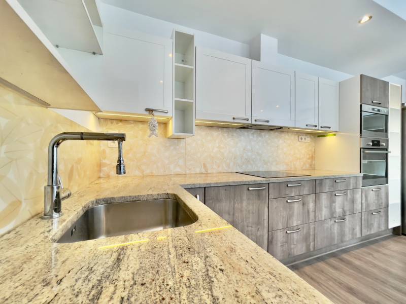 A kitchen in a 3-room apartment with a wooden decor floor and a granite countertop.