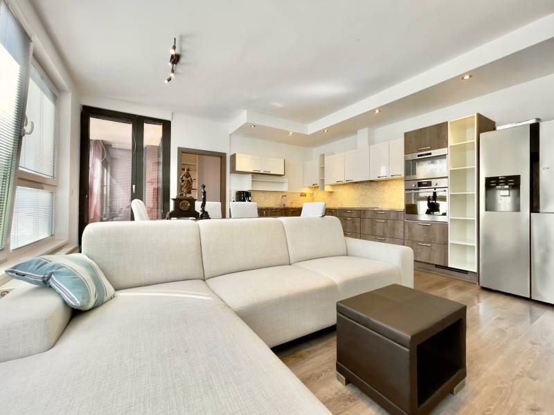 Living room of a three-room apartment with a white sofa and a kitchen unit.
