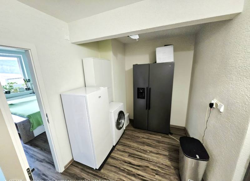 A kitchen in a 3-room apartment with a washing machine and a refrigerator. Floor with wooden decor.