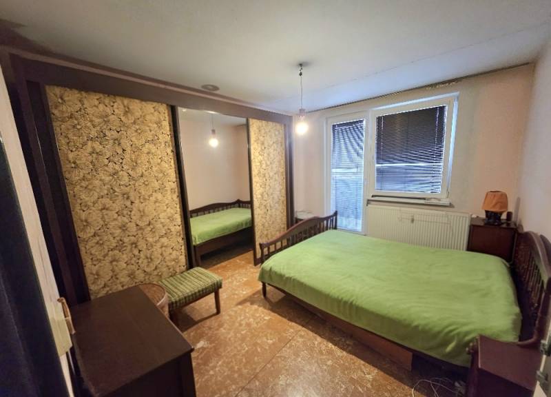 A bedroom in a 3-room apartment with a large wardrobe, a bed, and green bedding on the bed.