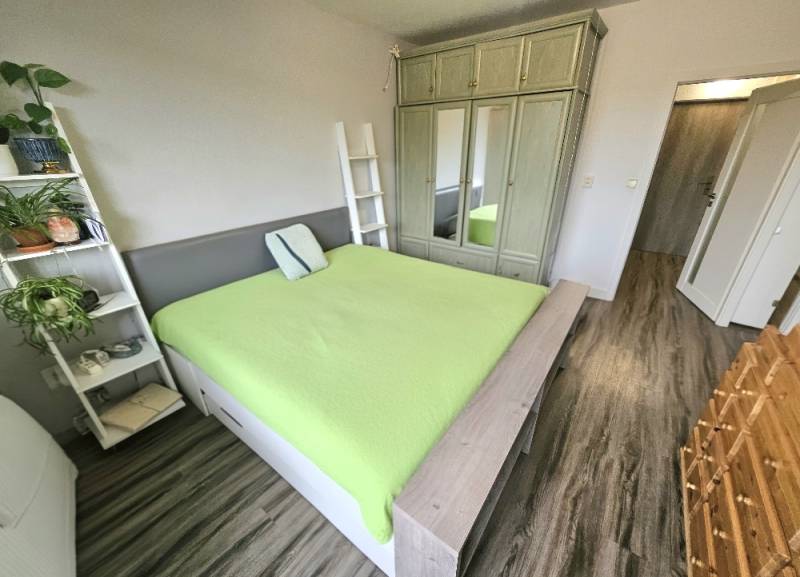 A bedroom in a three-room apartment with a wooden decor floor and a green bed.