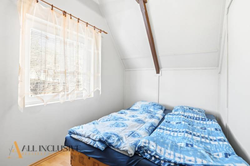 A bedroom in a cottage with an attic, two beds, a window with a curtain, and a floor with a wooden decor.