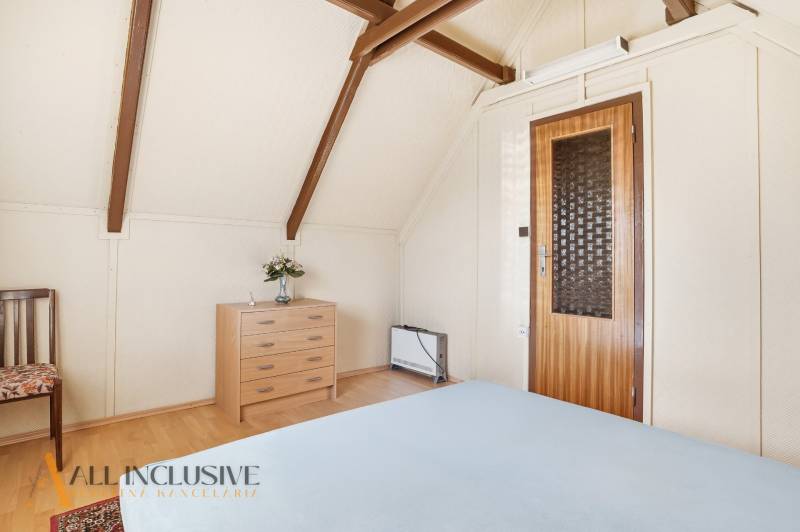 A room in a cottage with a chest of drawers, a chair, and a floor with a wooden decor.