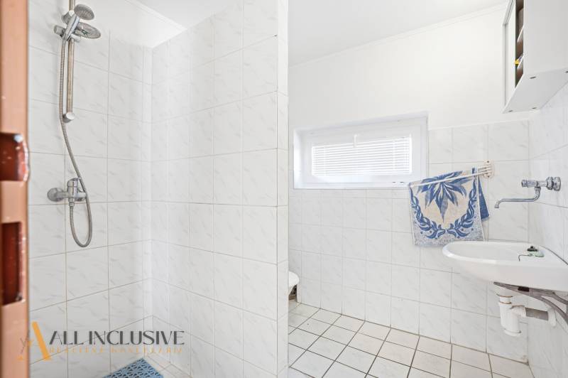 Bathroom in a cabin with tiles, shower, and sink, white walls with a window.