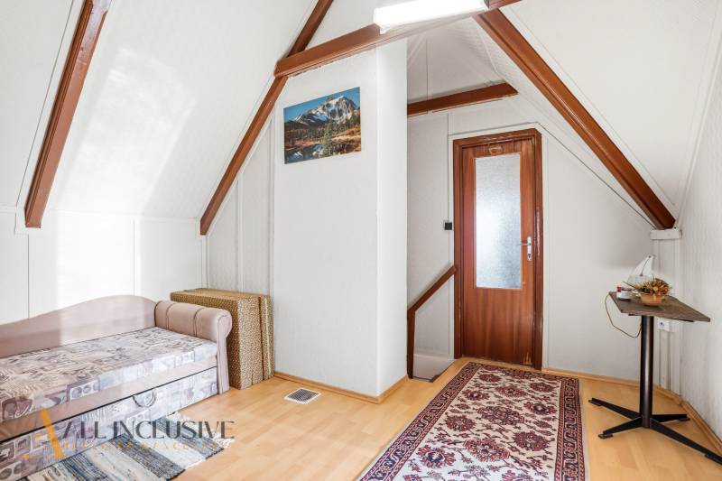 Attic room in a cottage with a chair, carpet, and table, wooden decor flooring.
