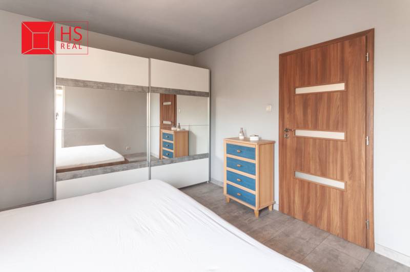 A bright bedroom with a large wardrobe, a mirror, and a wooden dresser in a family house.