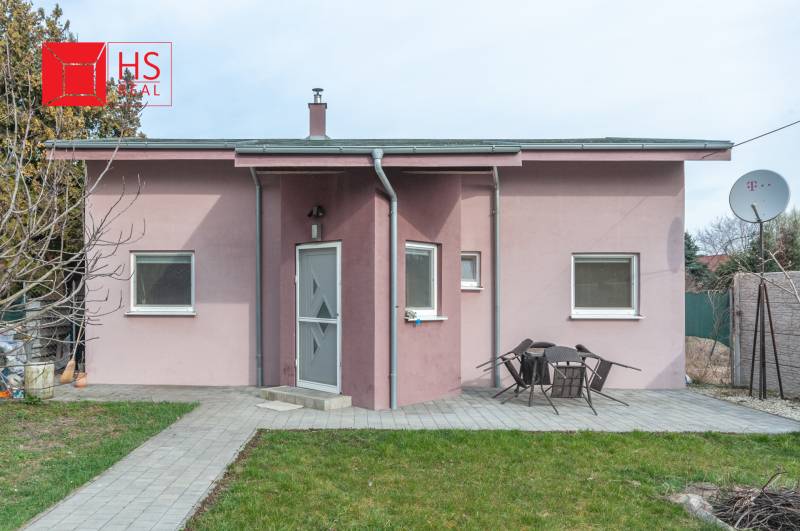 A family house in Šurany with a pink facade and a garden seating area on a paved walkway.