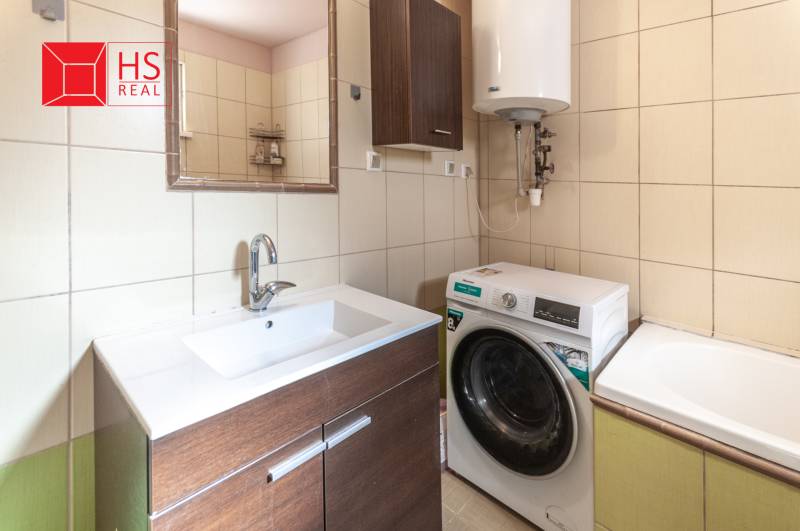 A bathroom in a family house with a washing machine, sink, mirror, and boiler on yellow tiles.