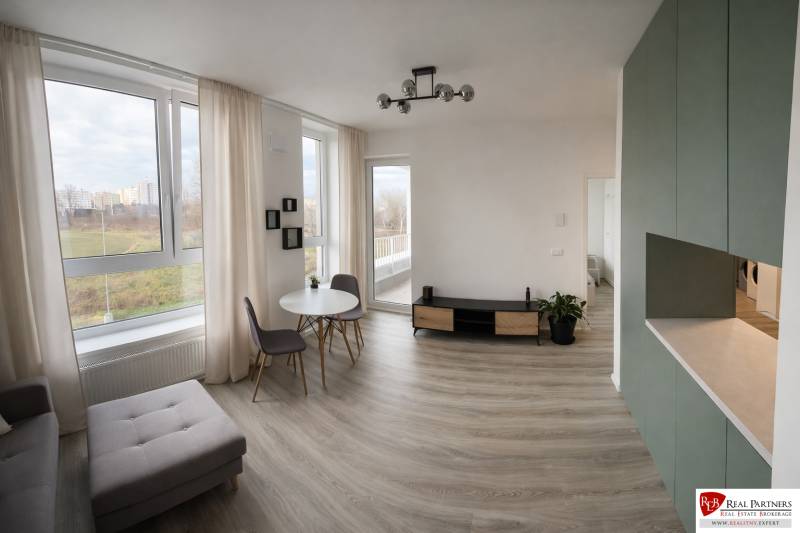 Living room in a two-room apartment with a wooden decor floor and large windows.