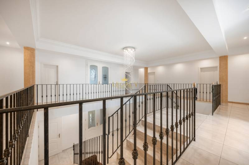 Interior of a family house with a staircase, railing, and chandelier.