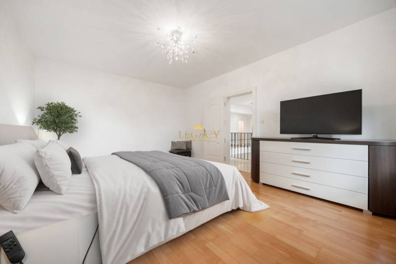 Bright bedroom with a bed, dresser, and television on a wooden floor.