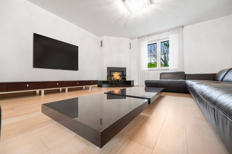 Living room with a black sofa, fireplace, and television, floor with wood decor.