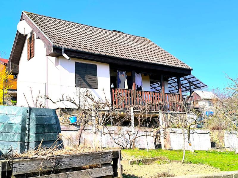 A cottage in Partizánske with a garden and terrace, surrounded by greenery and a blue sky.