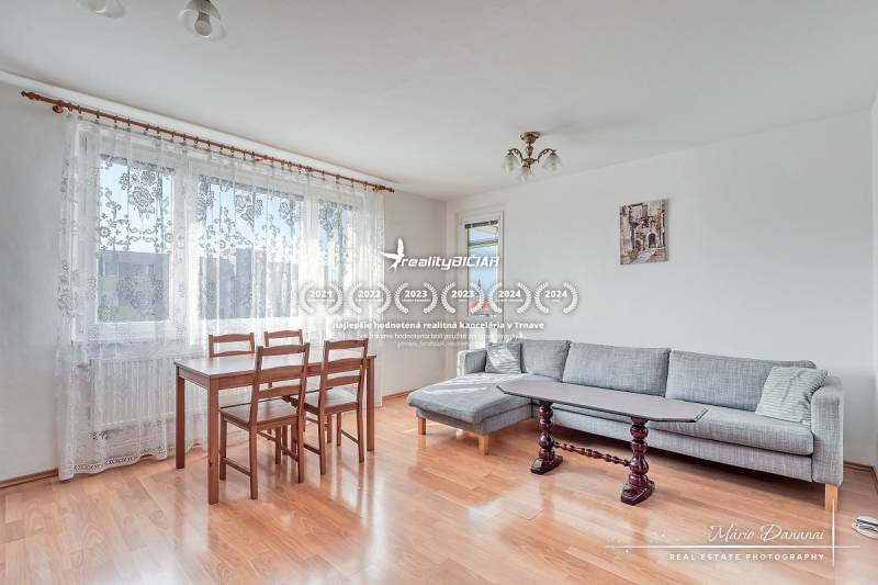 Living room in a three-room apartment with a wooden decor floor, dining table, and gray sofa.