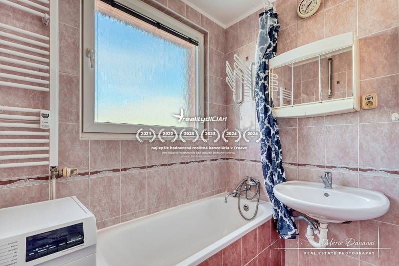 A bathroom in a 3-room apartment with a bathtub, sink, and washing machine, with tiled walls.